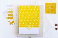 Top view of yellow floral notebook and Pantone cards on a white surface.