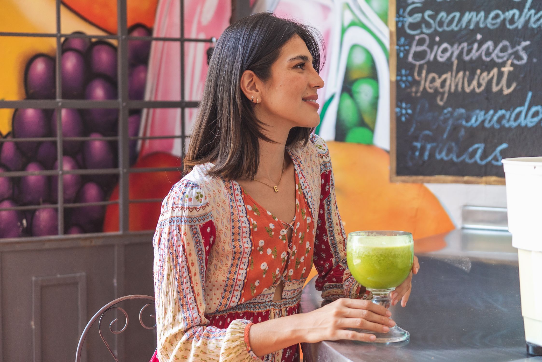 Mulher sorridente segurando um suco verde nutritivo, representando a hidratação e o suporte nutricional para a saúde da pele.