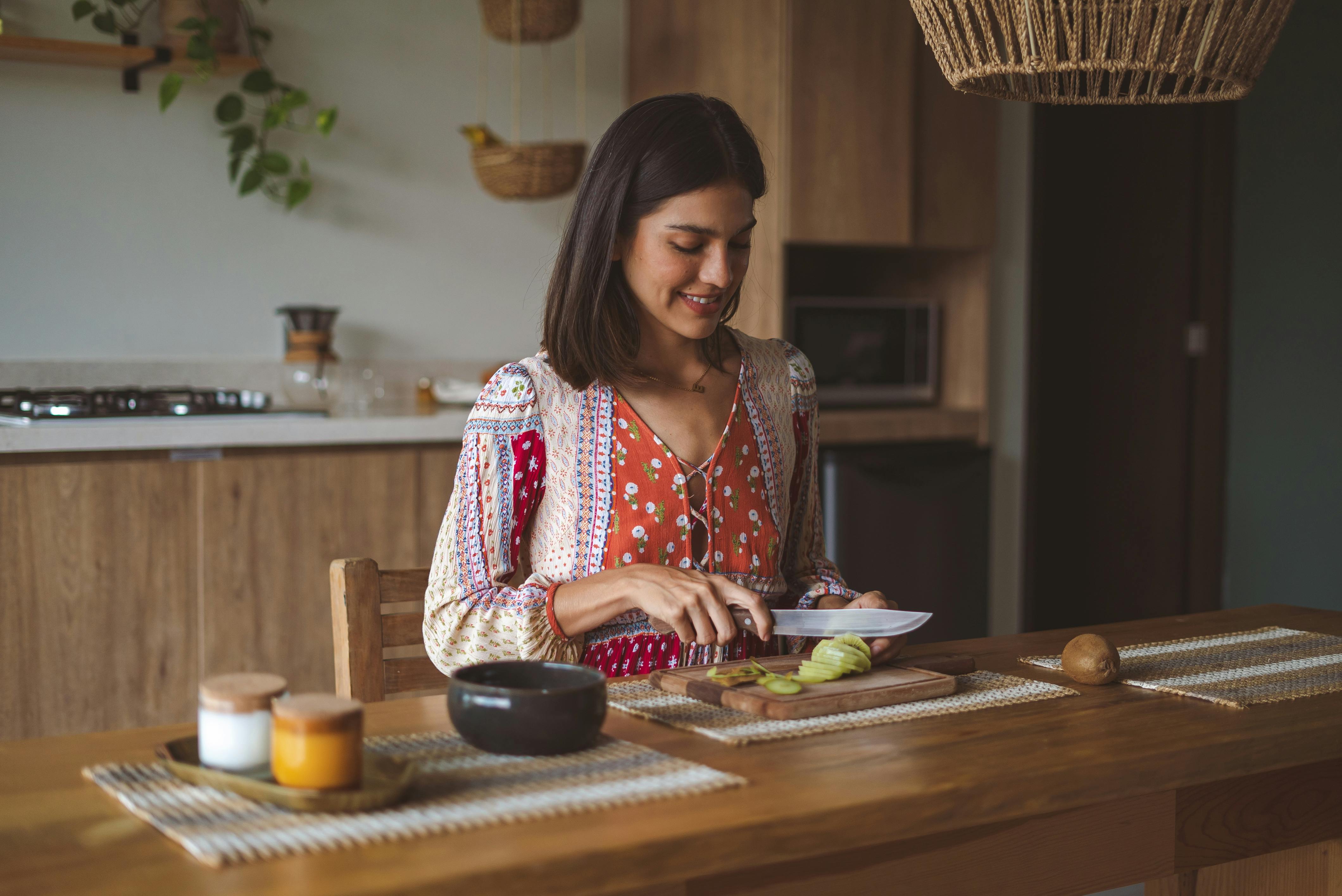 A smiling woman slices fruit on a kitchen counter, embracing a cozy and modern lifestyle.