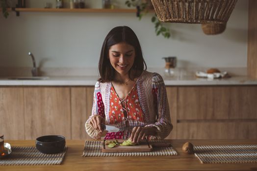 Smiling woman slicing vegetables on a chopping board in a warm, cozy kitchen setting.