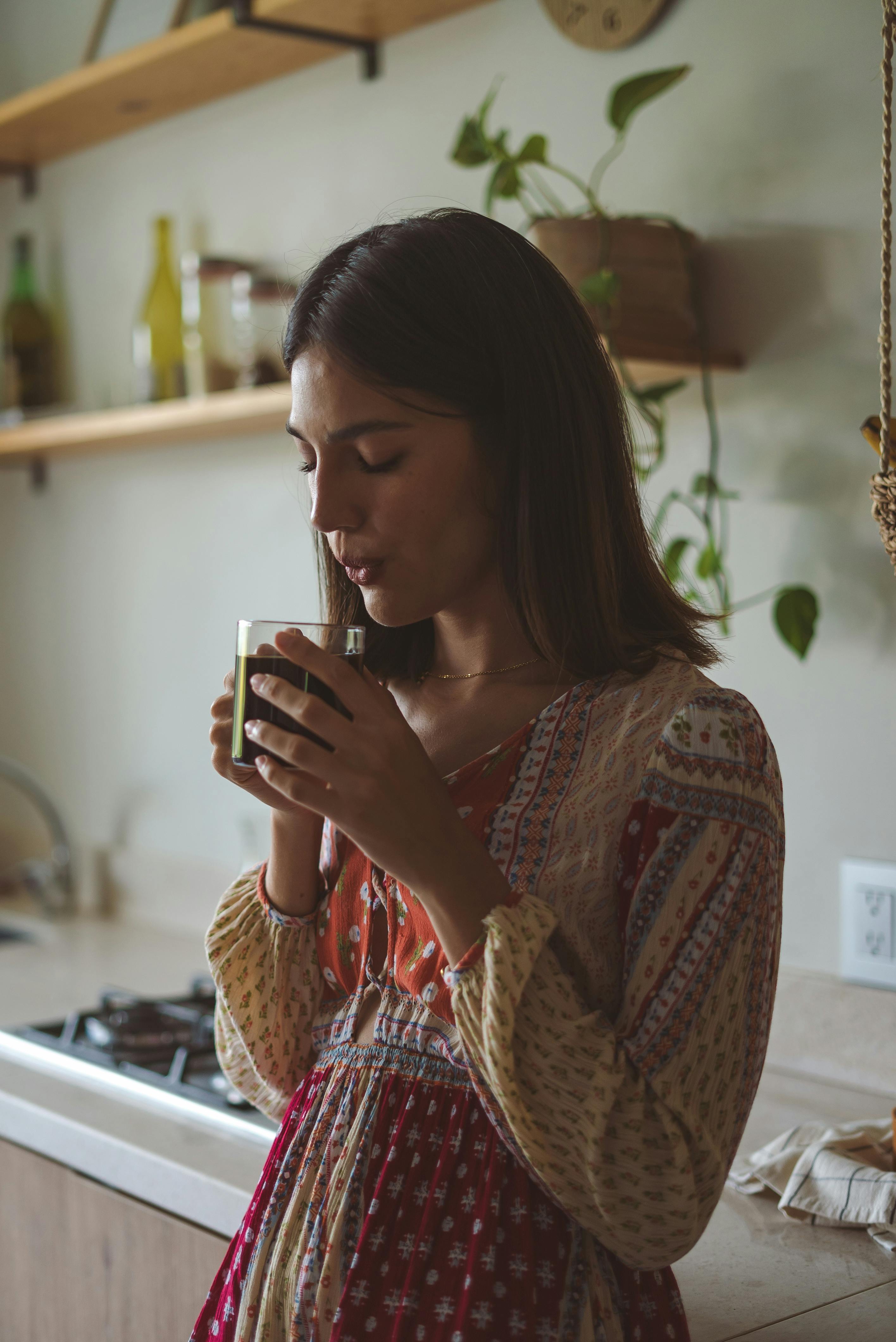 A young woman in a patterned dress enjoys a warm cup of coffee in a cozy kitchen.