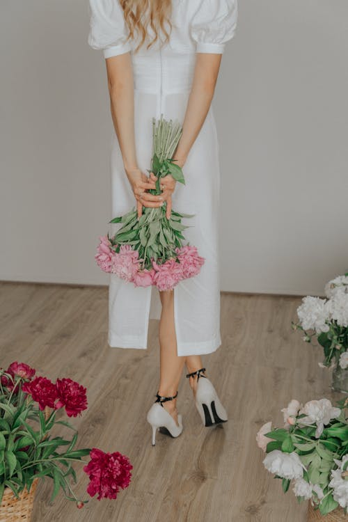 Woman in White Dress Holding a Bouquet of Flowers
