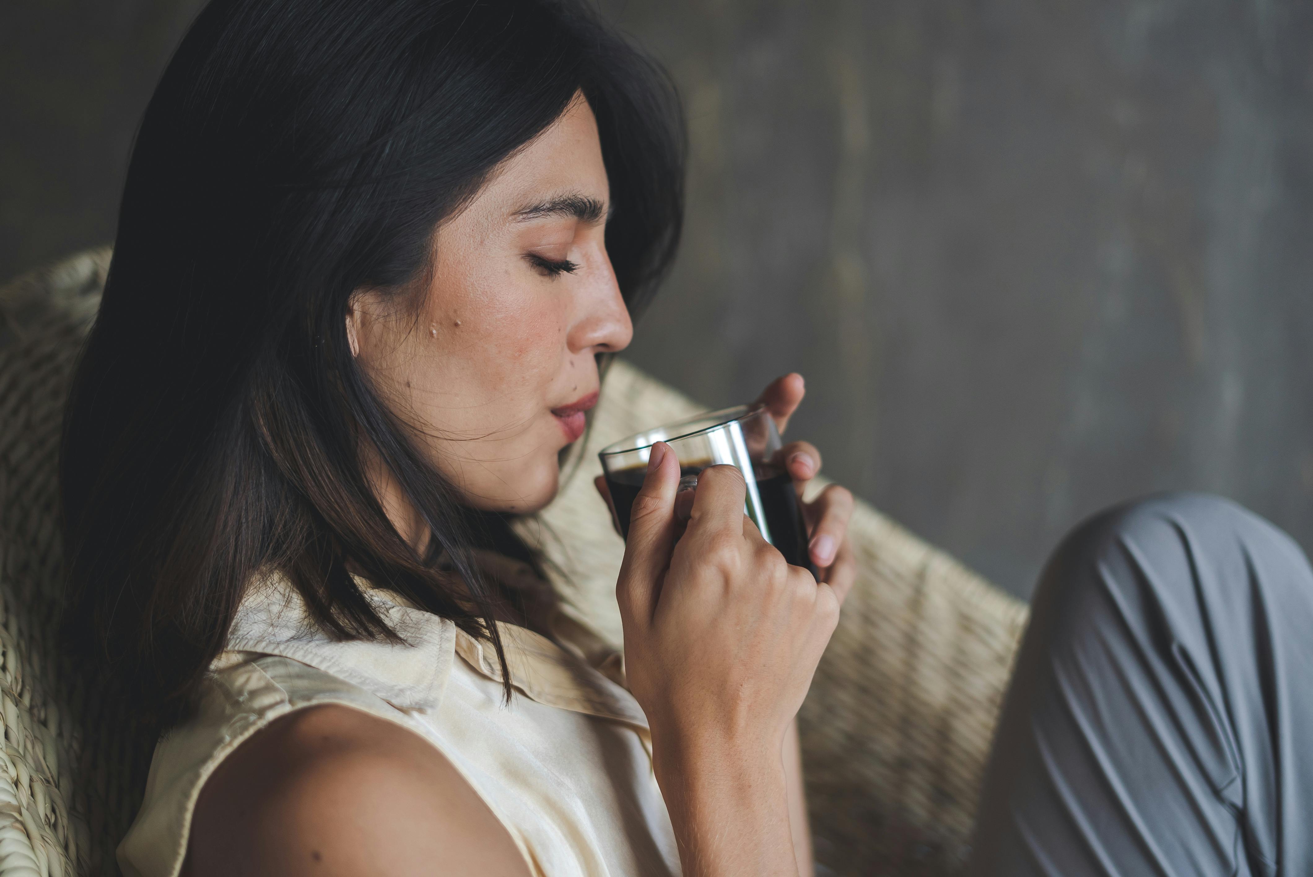 Woman savoring a cup of coffee while relaxing in a cozy chair indoors.