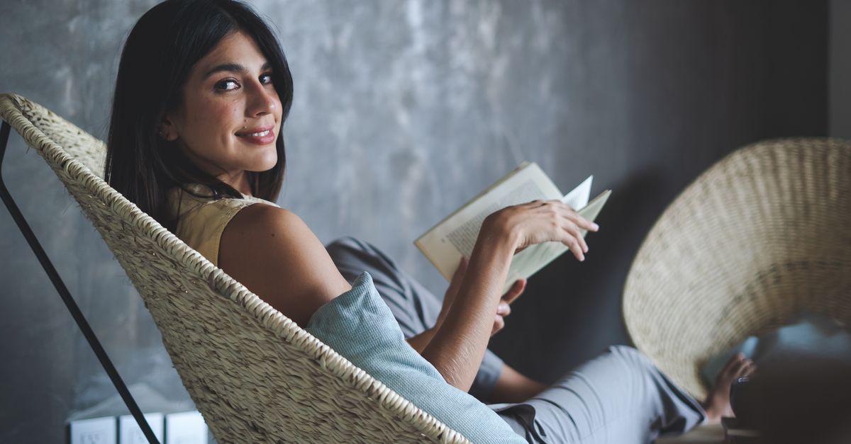 person reading a physical book in a cozy chair, natural light, calm atmosphere