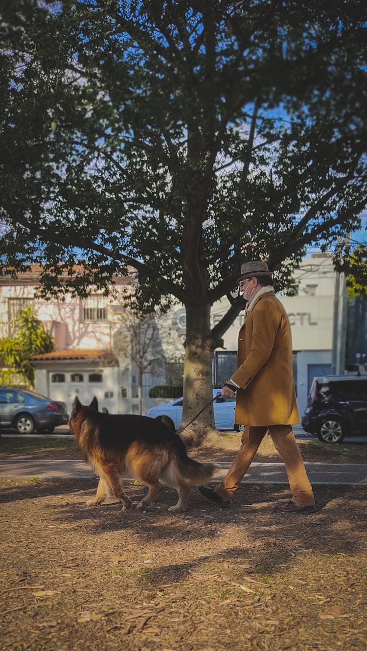 Man In Brown Coat And Pants Walking With A Dog 