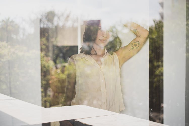 A Tattooed Woman In Sleeveless Top Behind The Glass Wall