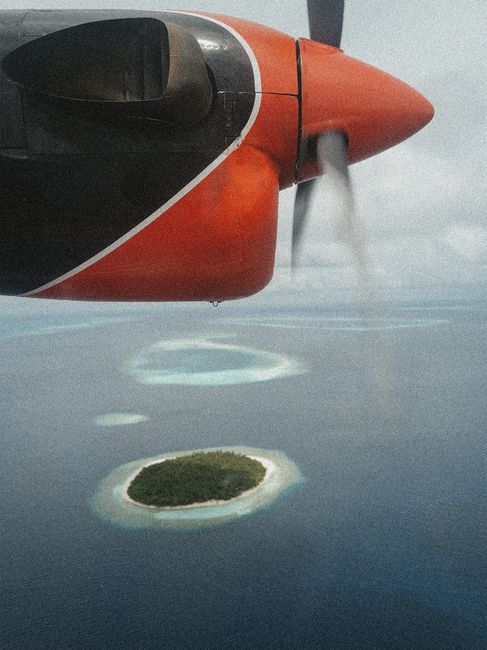 Scenic aerial view of a tropical island from an airplane window, showcasing clear blue waters and lush greenery.