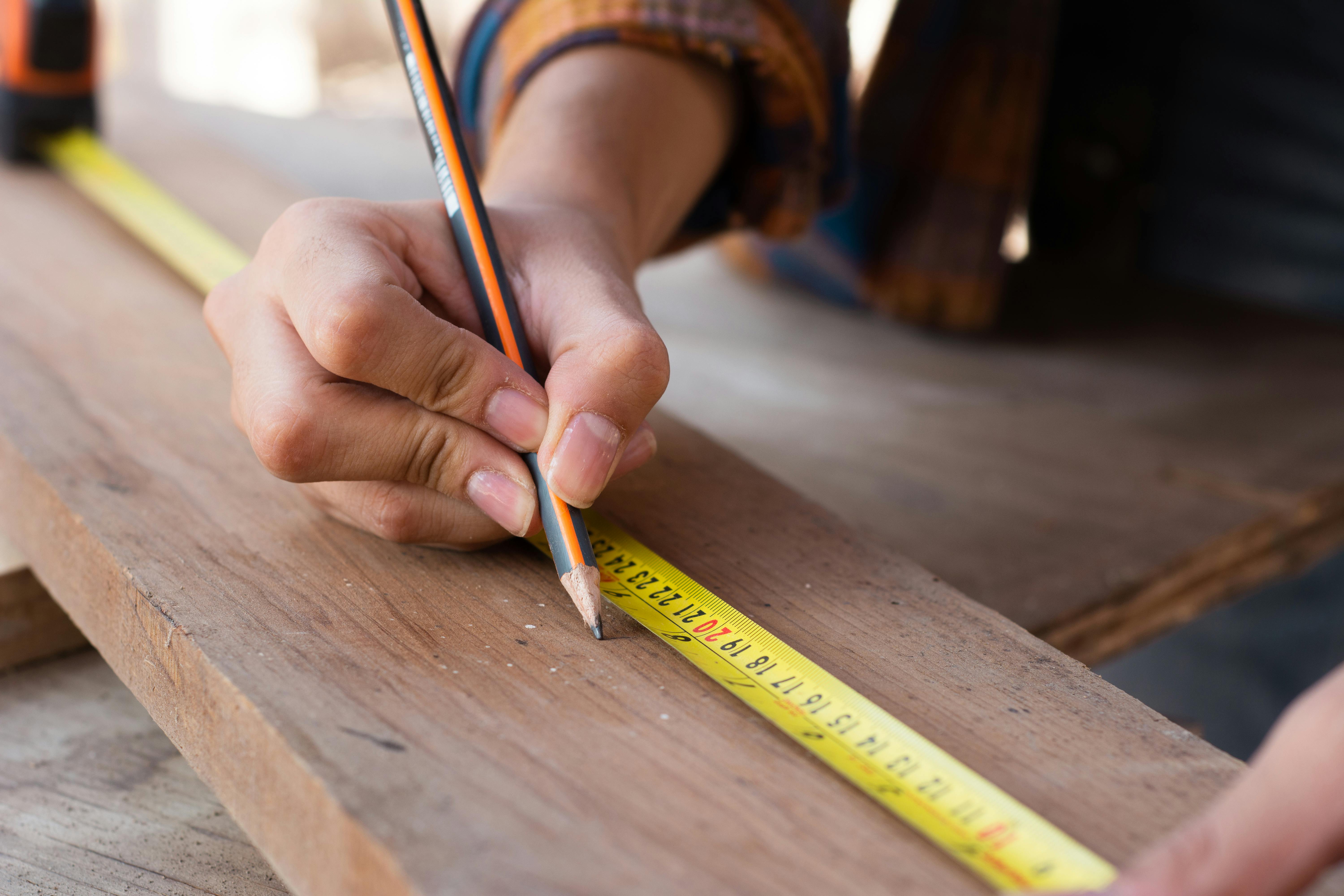 Close-up of hands using a measuring tape and pencil, highlighting precision in carpentry work.
