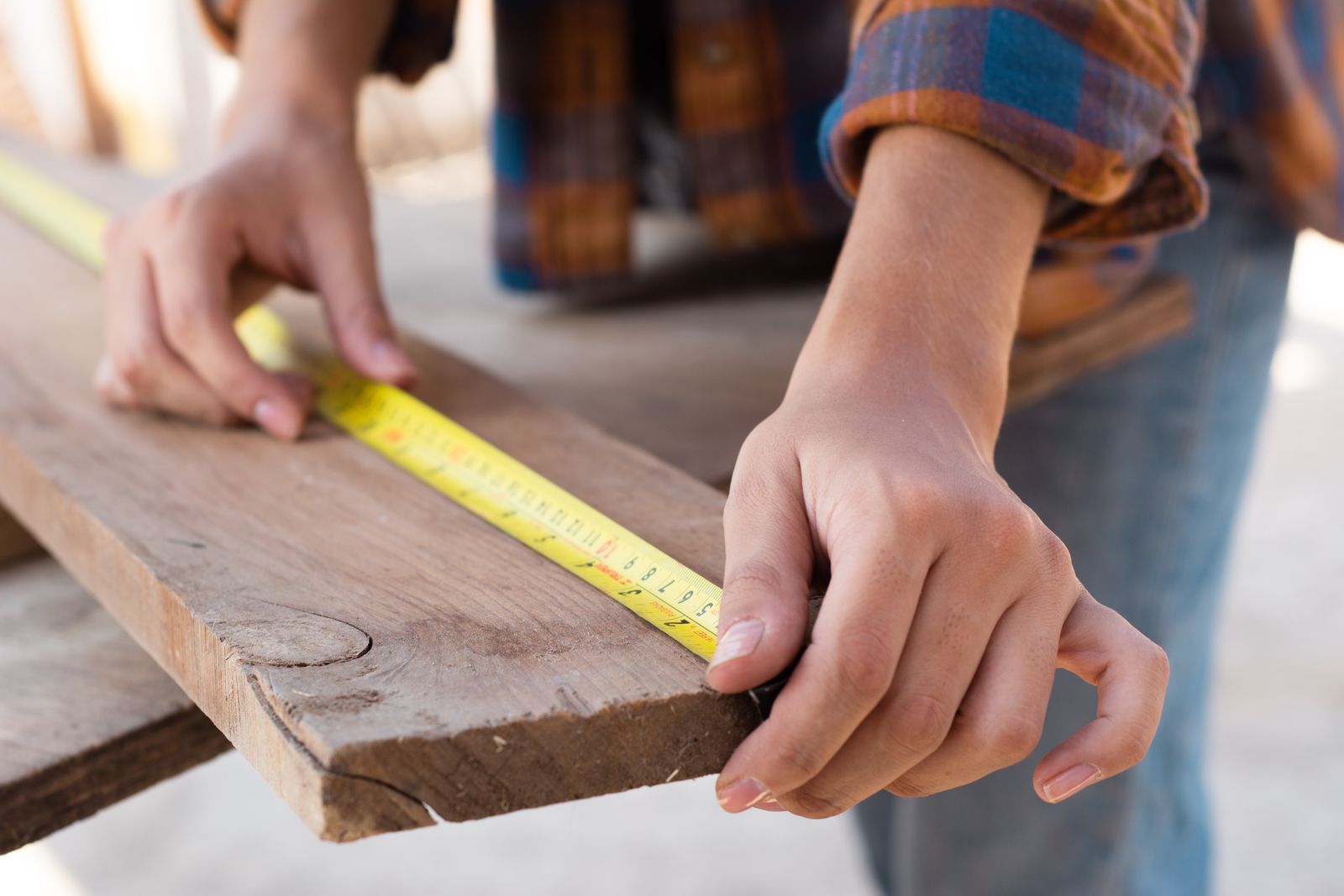 Hands measuring a wooden plank with a tape measure in a carpentry workspace