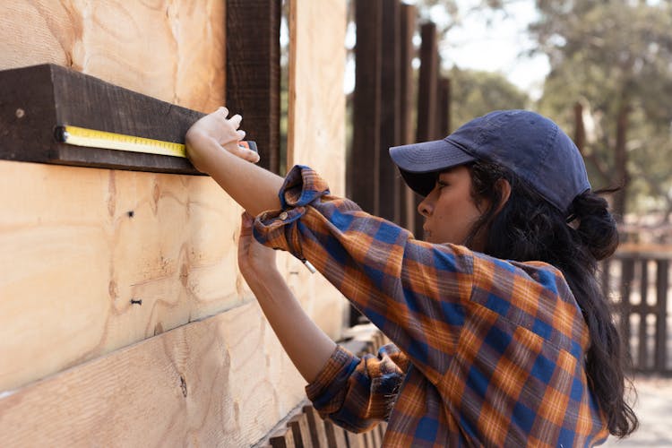 Woman In Cap And Plaid Long Sleeves Measuring A Wood 