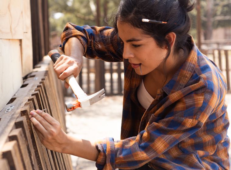 Carpenter using a hammer to fix a wooden fence