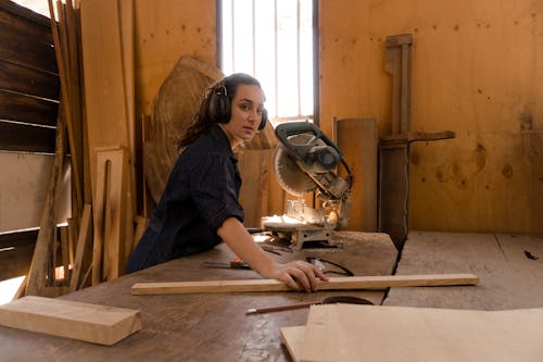 Free Woman Holding a Wood Plank in front of Miter Saw Stock Photo