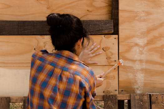 A woman in a plaid shirt expertly hammering a wooden plank. Empowerment in carpentry.