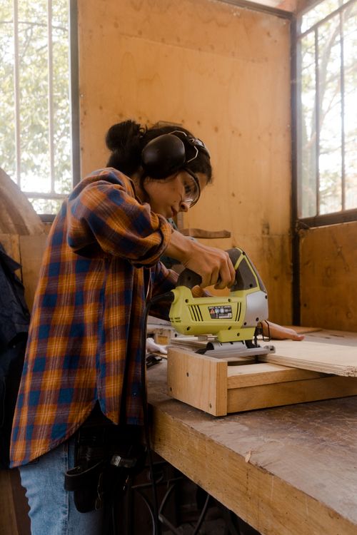 Free A female carpenter working with a power tool on a wooden plank in an indoor workshop setting. Stock Photo