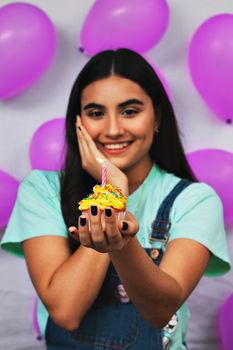 A cheerful woman holding a decorated cupcake with a lit candle, celebrating a birthday.