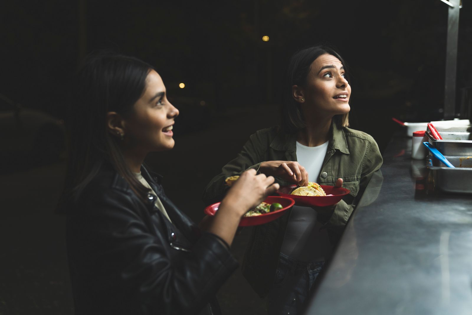 Two friends enjoying tacos at the Fuego Seoul truck counter at night