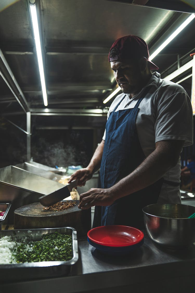 A Man Wearing An Apron While Chopping On A Wooden Board