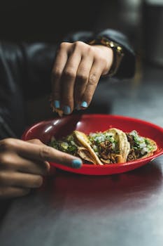 Close-up of a hand squeezing lime over authentic Mexican street tacos in a red plate.