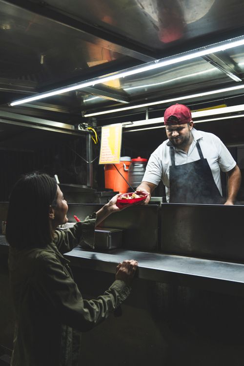 Free A street food vendor hands a taco to a customer at night, showcasing Mexican street cuisine. Stock Photo