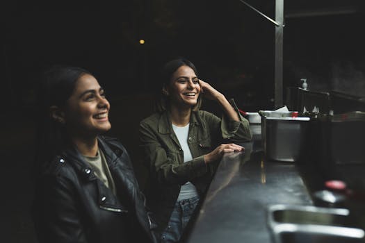 Two women smiling and enjoying their time at an outdoor taco stand during the night.