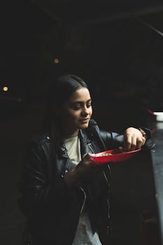 Young woman in a leather jacket enjoys Mexican street food outdoors at night.