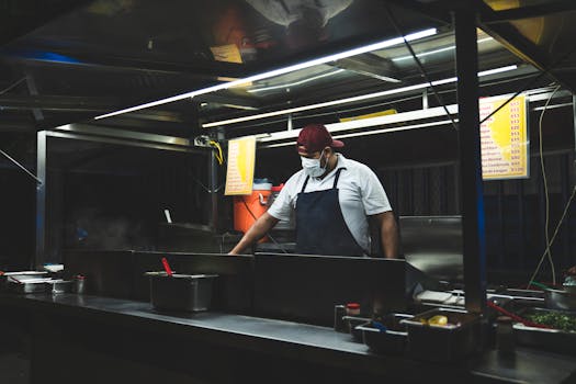 A street vendor in apron prepares tacos at a night food booth, showcasing Mexican cuisine.