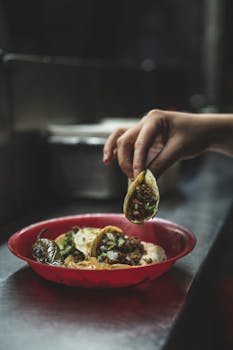 Close-up of fresh Mexican tacos in a red plate with a hand picking one