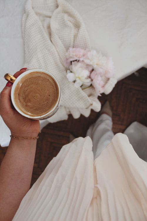 Free Hand holding coffee cup in soft morning setting with flowers and blanket. Stock Photo