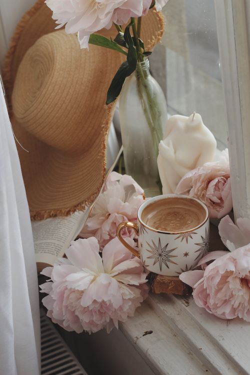 Free A serene setup by the window featuring a cup of coffee, pink peonies, and a straw hat. Stock Photo