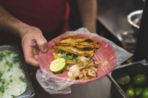Free Hand holding a plate of authentic Mexican tacos with lime and onions, showcasing delicious street food. Stock Photo