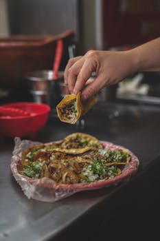 Close-up of a hand holding a delicious taco with a plate of assorted tacos in the background.
