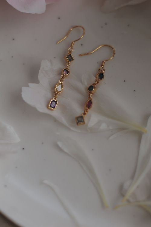 Free Close-up of luxurious gold earrings with colorful gemstones on white petals. Stock Photo