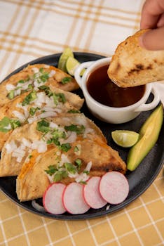 Close-up of delicious Mexican tacos with dipping sauce, garnished with radish and lime on a table.