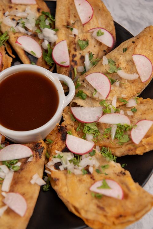 Free Mouth-watering authentic Mexican tacos garnished with onions, radishes, and cilantro served with a dip. Stock Photo