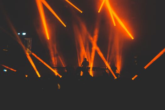 A DJ on stage with striking orange light beams creating a captivating club atmosphere.