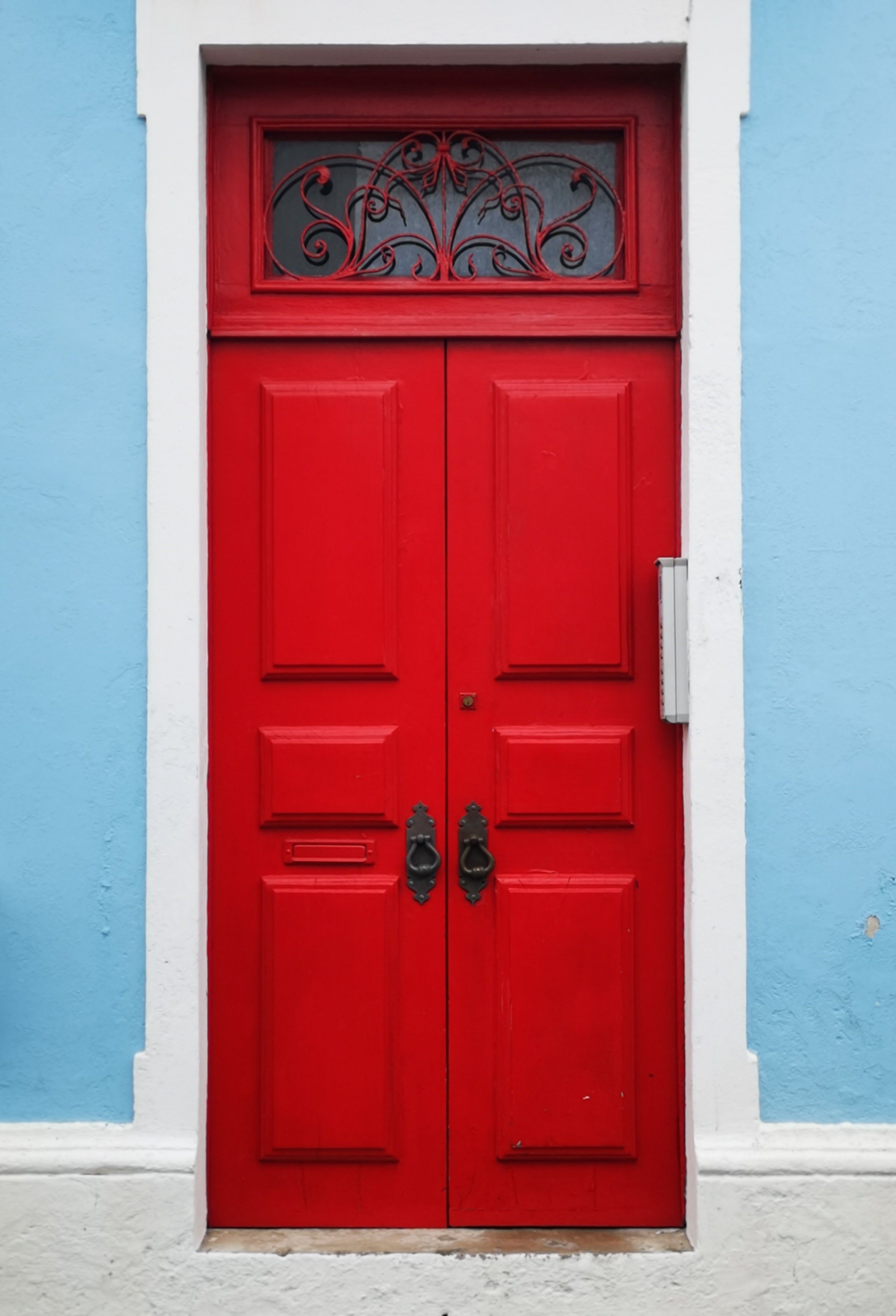 A classic red wooden door with ornate design set in a pastel blue wall exterior.