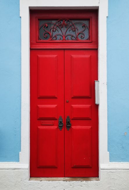 A classic red wooden door with ornate design set in a pastel blue wall exterior.