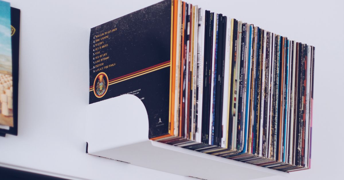 A neat stack of vinyl records on a minimalist white wall shelf.