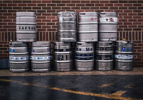 Free Row of metallic beer kegs stacked outside a brick wall, showcasing brewing industry. Stock Photo