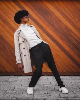 Fashionable young man with afro hair stylishly leans against a wooden wall.