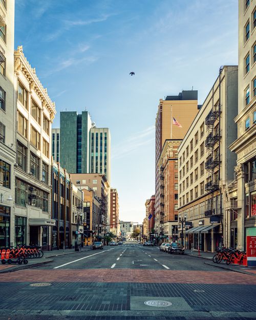 Free Wide empty urban street with tall buildings under a clear blue sky. Stock Photo