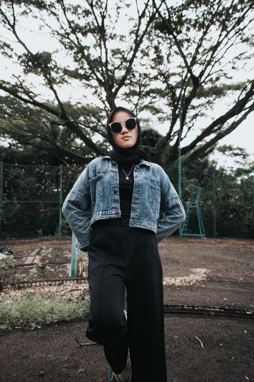 Free Fashionable woman in sunglasses and denim jacket posing outdoors with trees in the background. Stock Photo