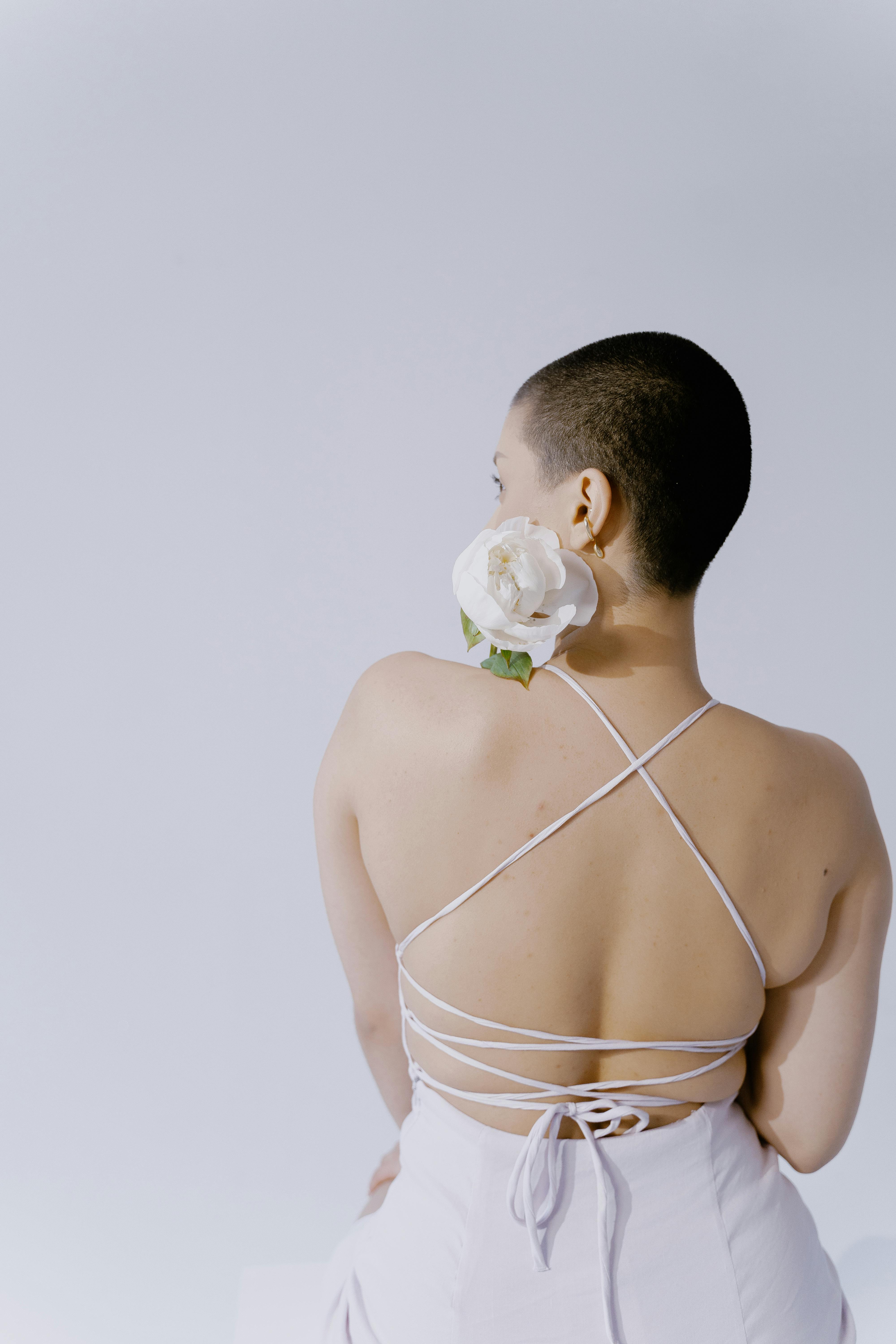 Artistic shot of a woman in a backless dress with a white rose. Ideal for fashion or lifestyle themes.