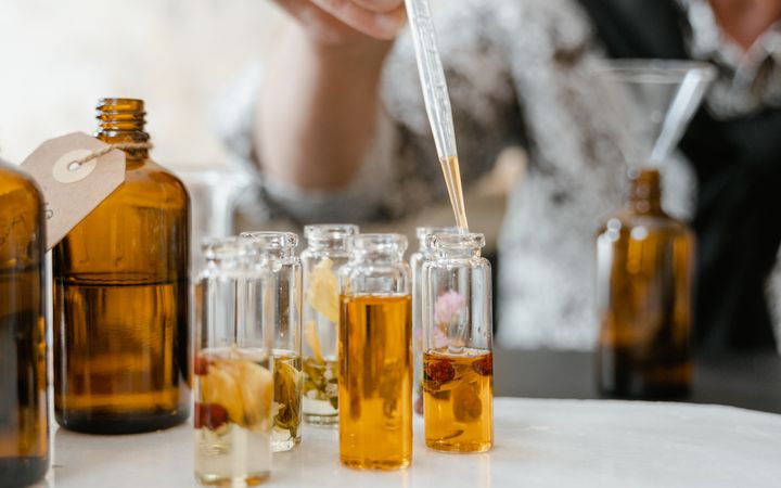 A person blends aromatic essences using a dropper for bespoke fragrances, emphasizing artisanal craftsmanship.