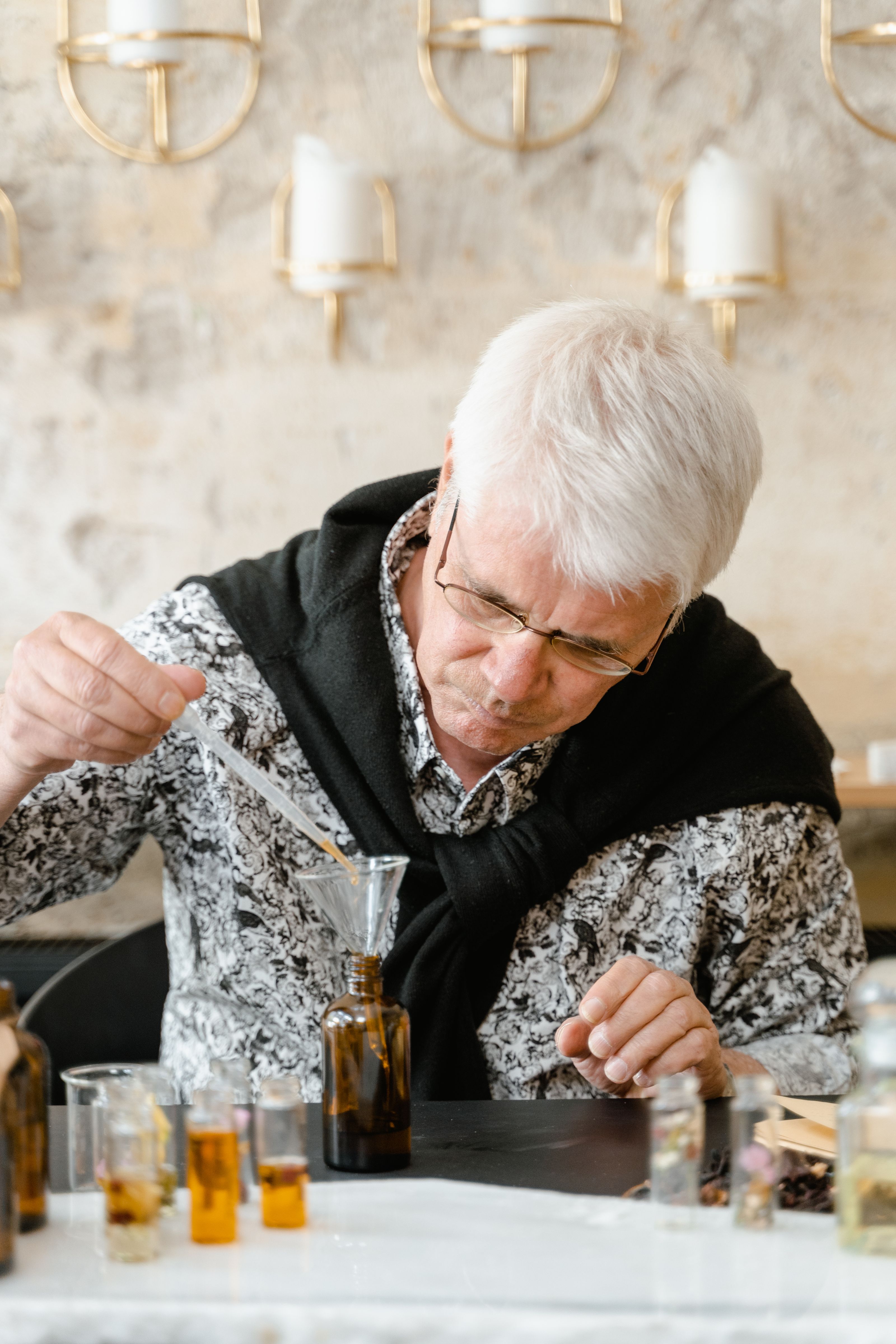 Homem idoso criando cuidadosamente uma mistura de perfume em um espaço de trabalho interno com várias garrafas.
