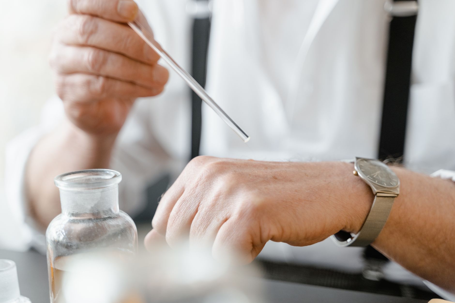 Close-up of a man using a dropper to apply fragrance on his wrist indoors.