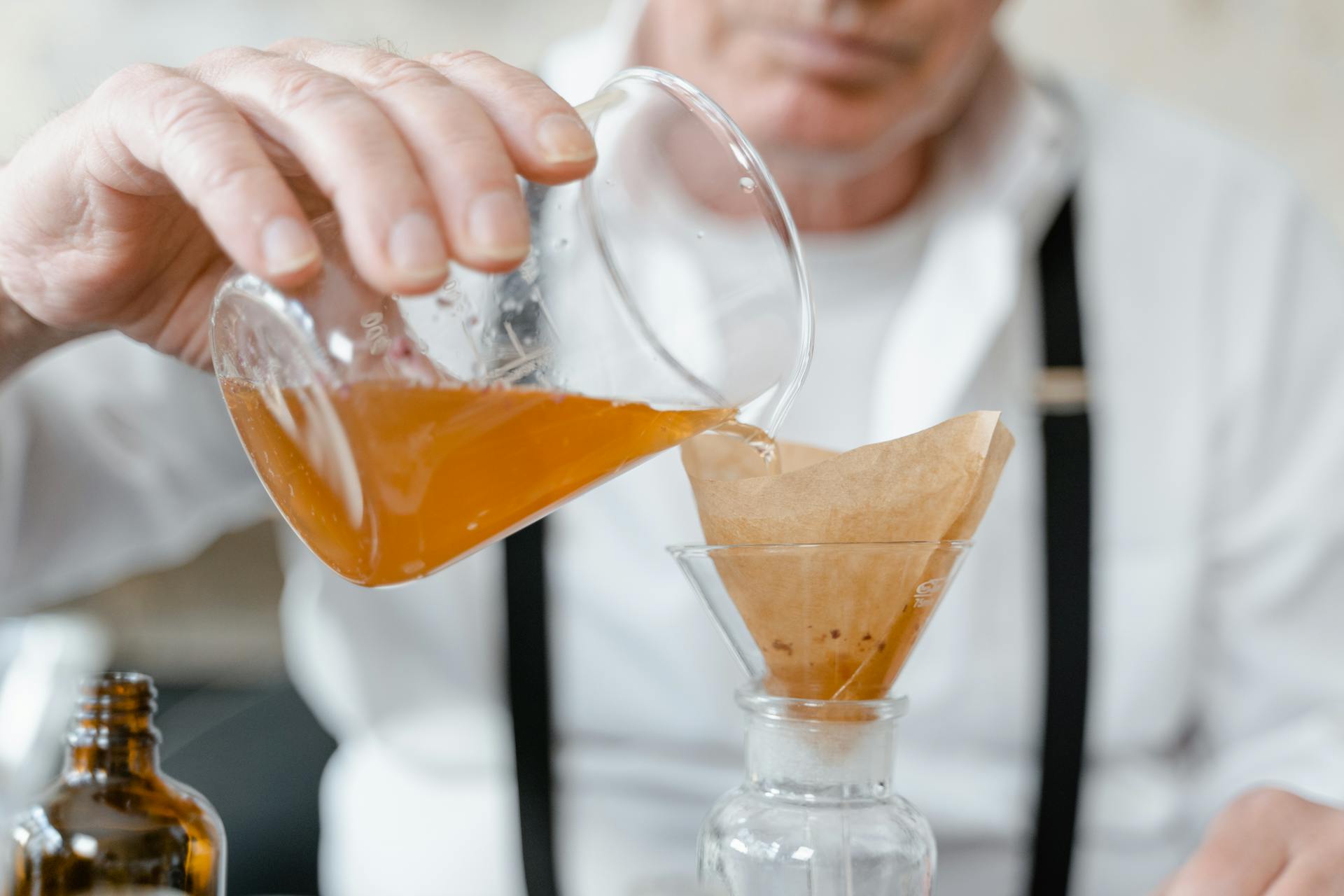 A Man Pouring Liquid From a Breaker into a Glass Funnel