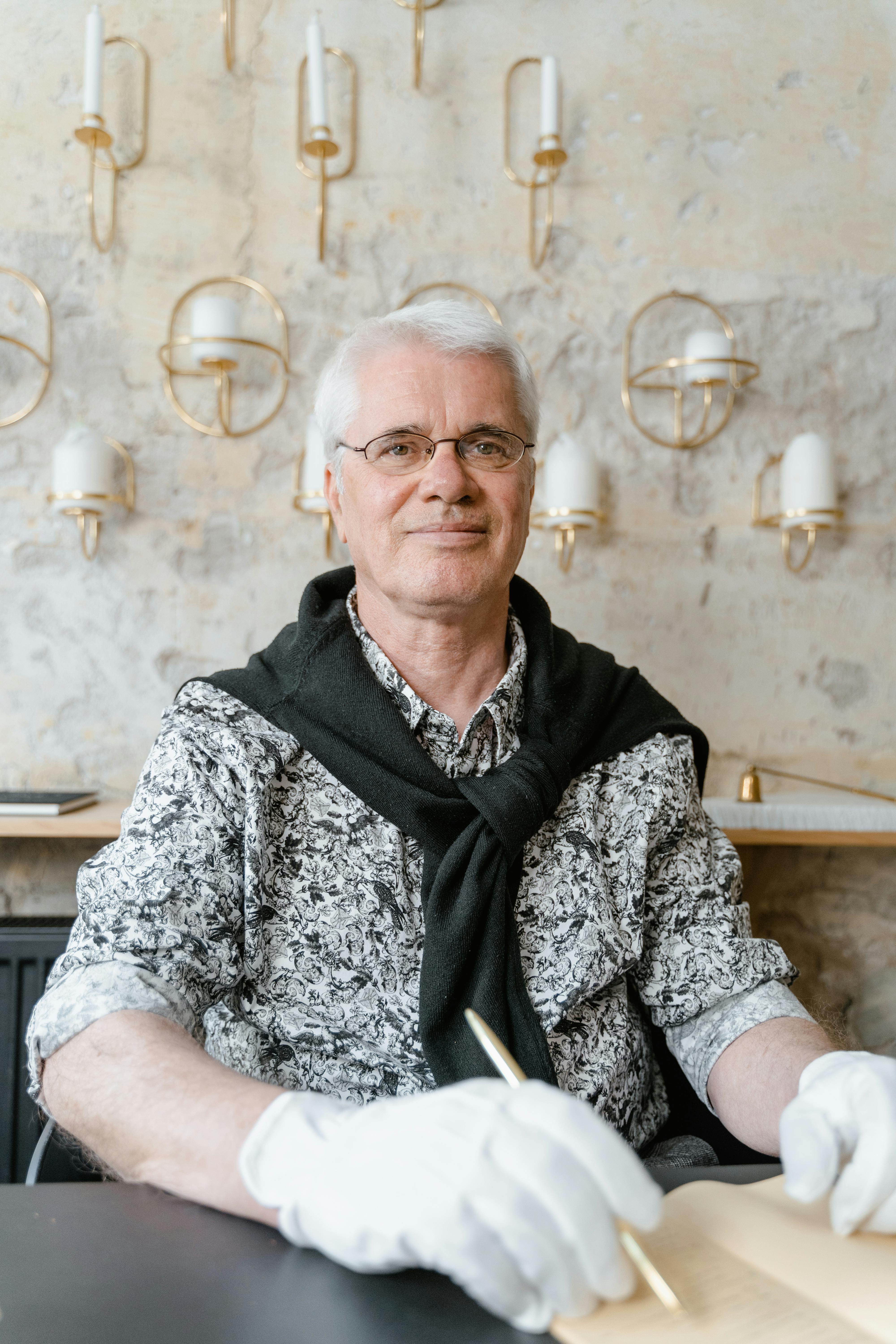 Elderly man with glasses taking notes in a stylish room with artistic wall lamps.