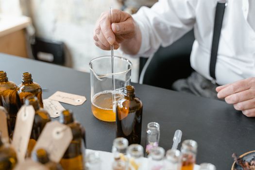 A detailed view of a scientist's hand mixing liquid in a beaker with glass bottles around on a lab table.