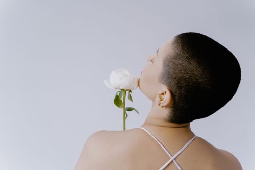 Free Elegant portrait of a woman enjoying the scent of a white flower against a minimal background. Stock Photo